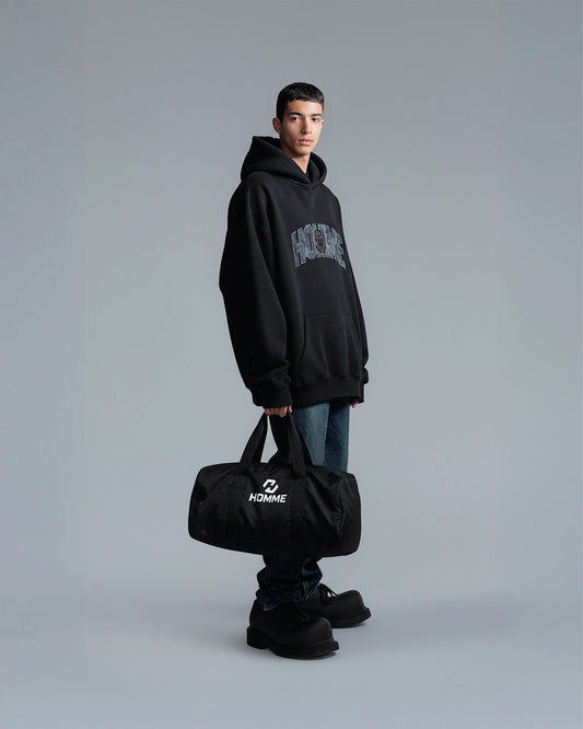 Model carrying the Not Guilty Homme sport bag, demonstrating its scale and function as a modern gym accessory in black.