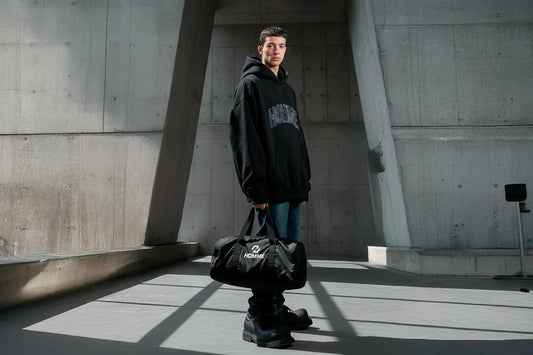 NOT GUILTY HOMME AW25 campaign — model with Lightweight Sport Bag in a concrete setting