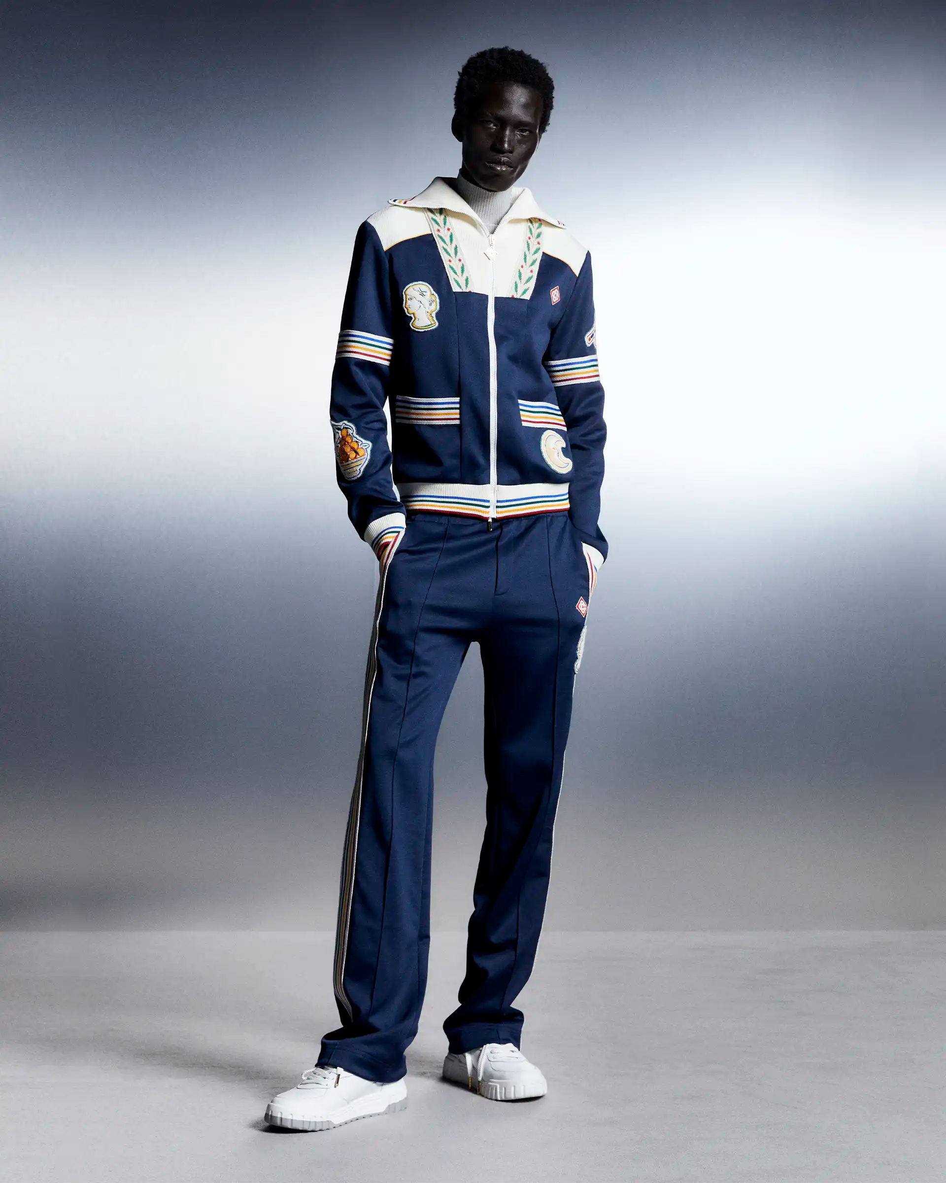 Model wearing Casablanca navy blue tracksuit set with embroidered patches and laurel collar detail.