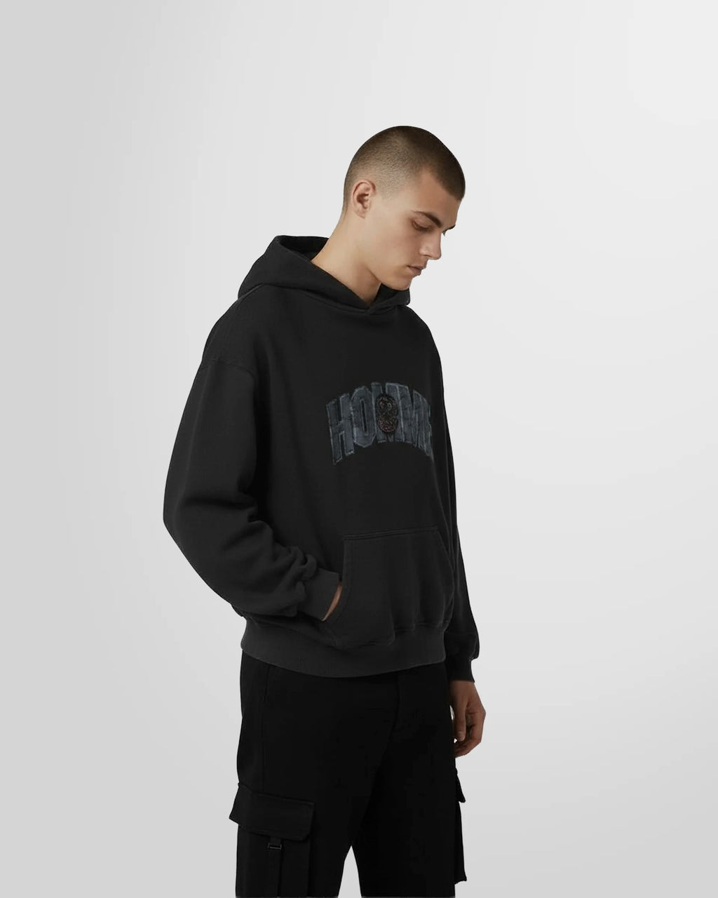 View from the side of a model wearing the Not Guilty Homme College Hoodie in black with varsity HOMME graphic in front.