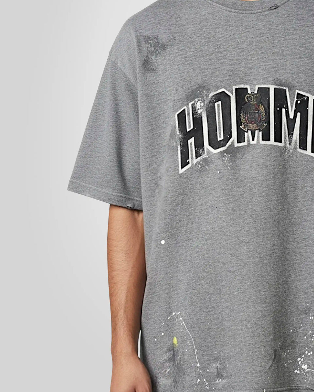 Close‑up of the tonal embroidered patch with distressed textured fill and the  hand‑made paint stains on the misty grey t‑shirt.