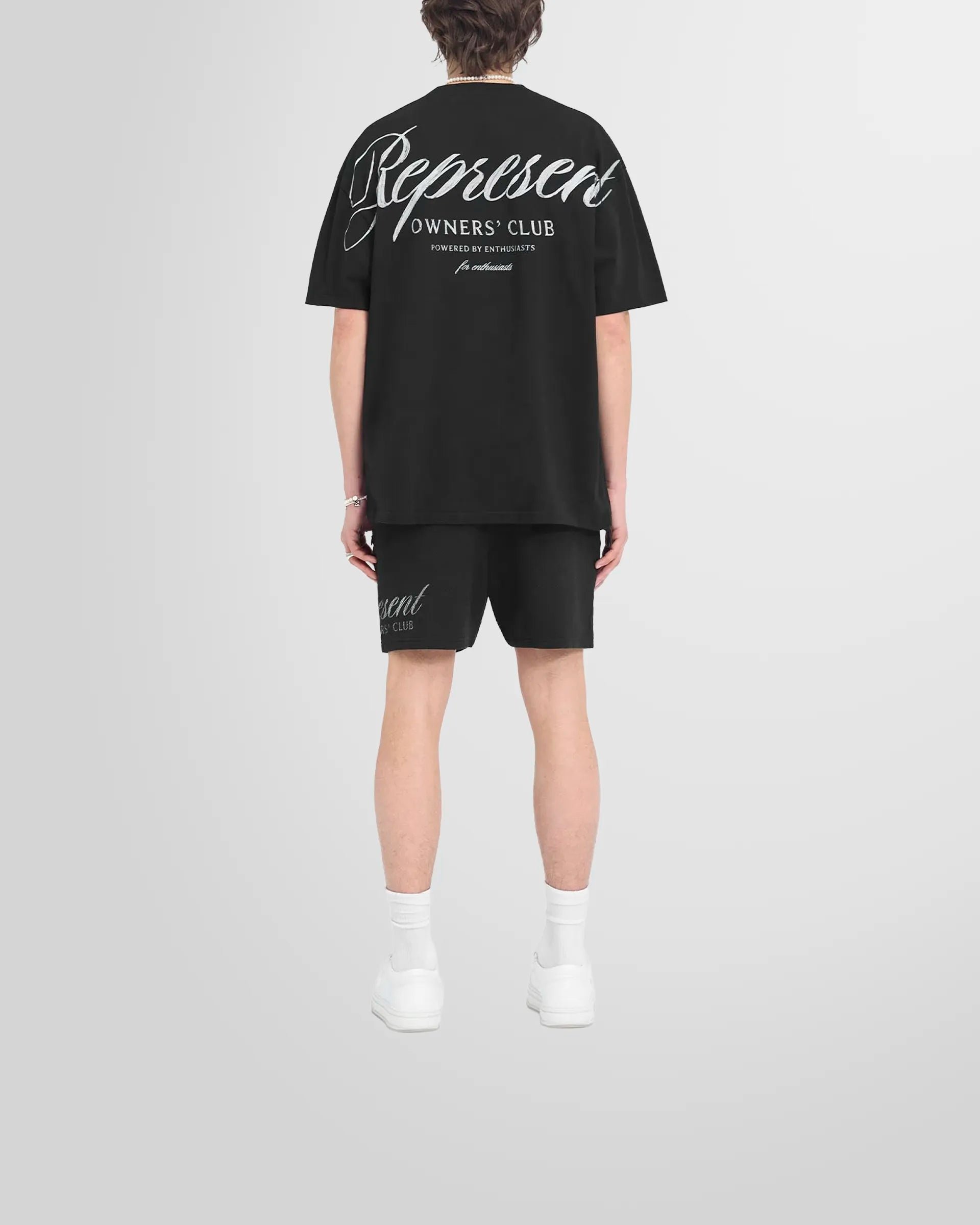 Back od a model wearing the oversized Represent Owners Club Script T-Shirt in black.