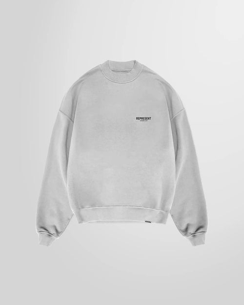 Front view of the Represent Owners' Club Sweater in ash grey, showing the black chest print.