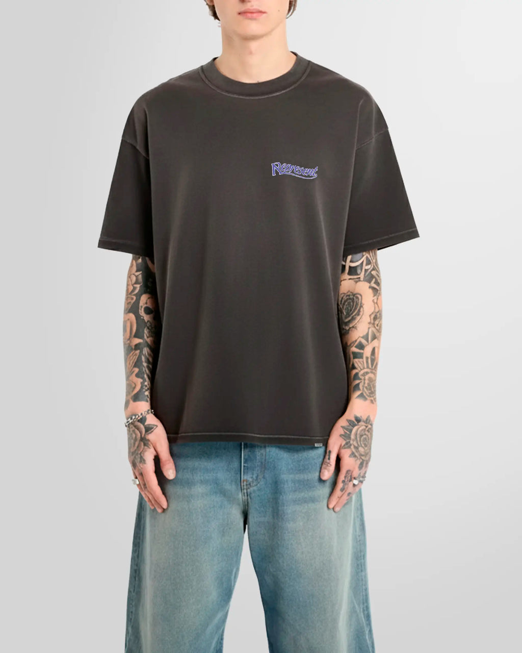 Model wearing the Represent Showcasing T‑Shirt in Stained Black with chest script logo.
