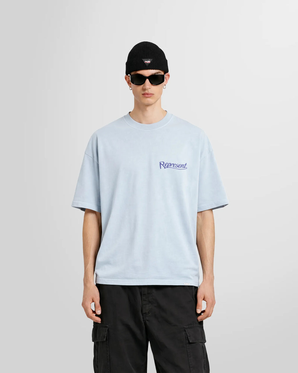 Model wearing the Represent Showcasing T‑Shirt in Cloud blue with small script logo at chest.