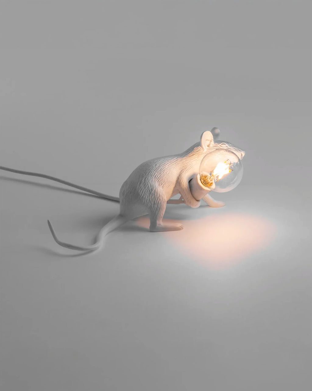 The Seletti Lie Down Mouse Lamp turned on, casting a warm and ambient glow in a dimly lit room.