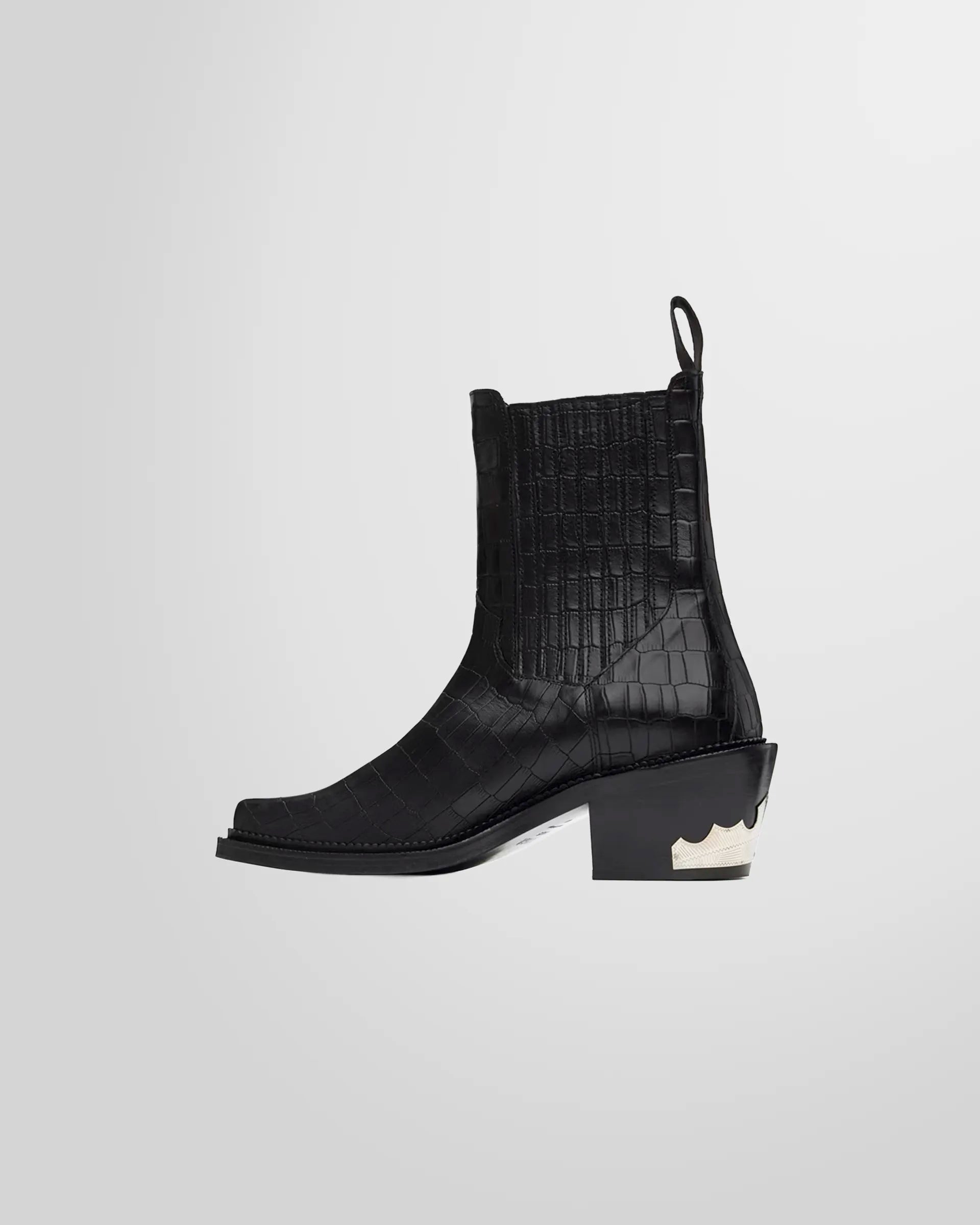 Side view of the ornate silver-tone Western hardware on the heel of the Toga Virilis black Chelsea boots.